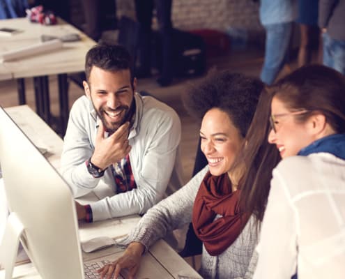 coworkers smiling while working on a project on a computer