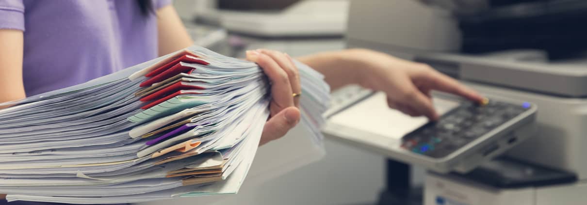 May Blog 3 Image closing up of woman holding a stack of papers and using a copy machine
