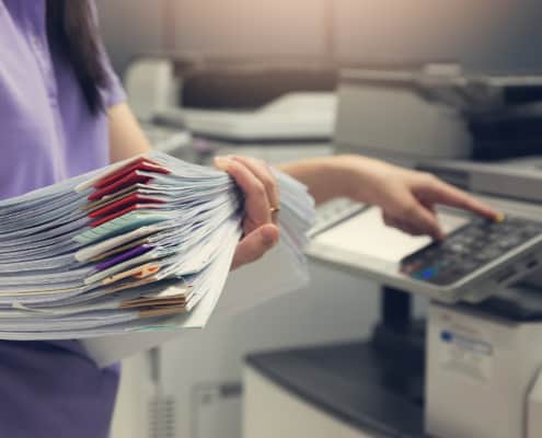 closing up of woman holding a stack of papers and using a copy machine